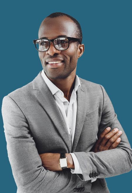 Man in a gray suit and glasses smiles with arms crossed against a blue background.